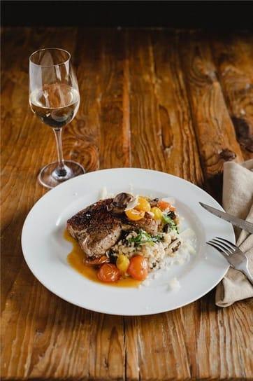 An entree beside a white wine on a rustic wood table